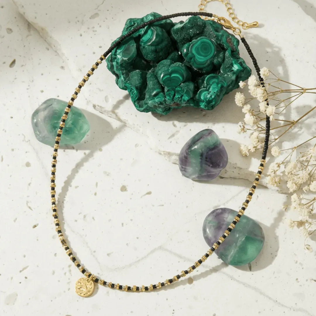 Necklace with green and purple beads on a textured surface with a green stone and white flowers.