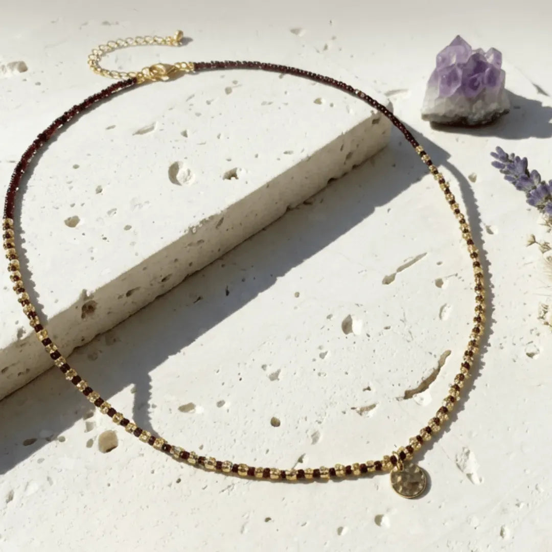 Necklace with brown and gold beads on a textured surface with a crystal and flower.