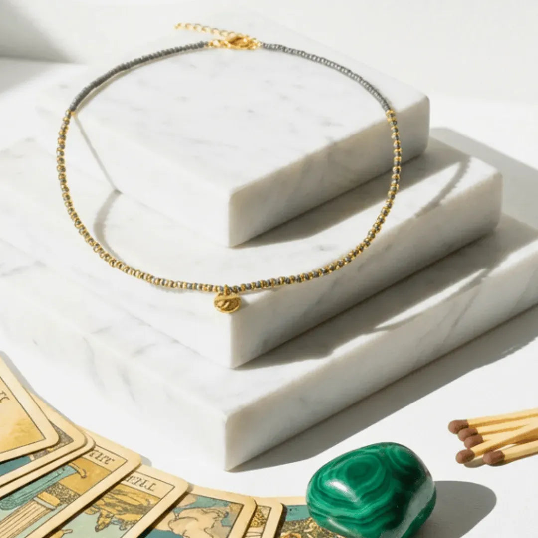 Gold necklace on a marble surface with tarot cards and a green stone.