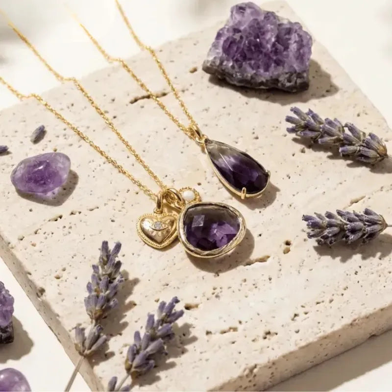 Gold necklaces with purple gemstones on a stone surface with lavender flowers