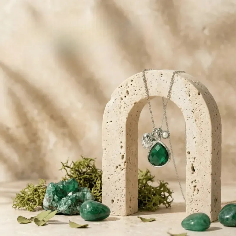 Necklace with a green teardrop pendant on a stone arch with green stones and plants around.