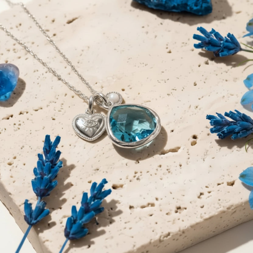 Silver necklace with a blue pendant on a stone surface with lavender flowers