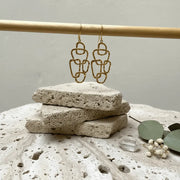 Gold chain earrings on a stone surface with a neutral background