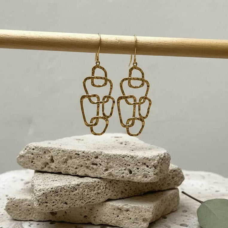Gold chain earrings on a stone surface with a neutral background