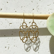 Gold earrings on a wooden stick against a light background