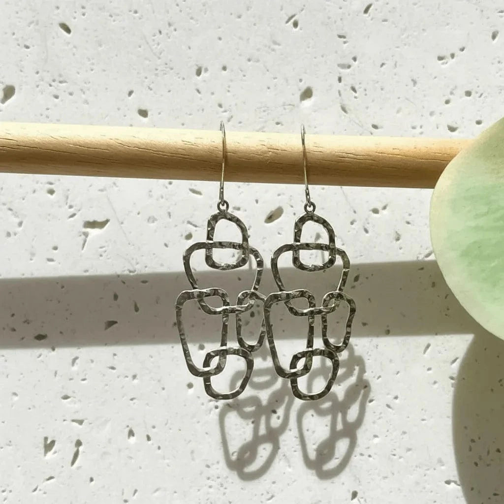 Silver chain-style earrings hanging from a wooden rod on a textured white surface.