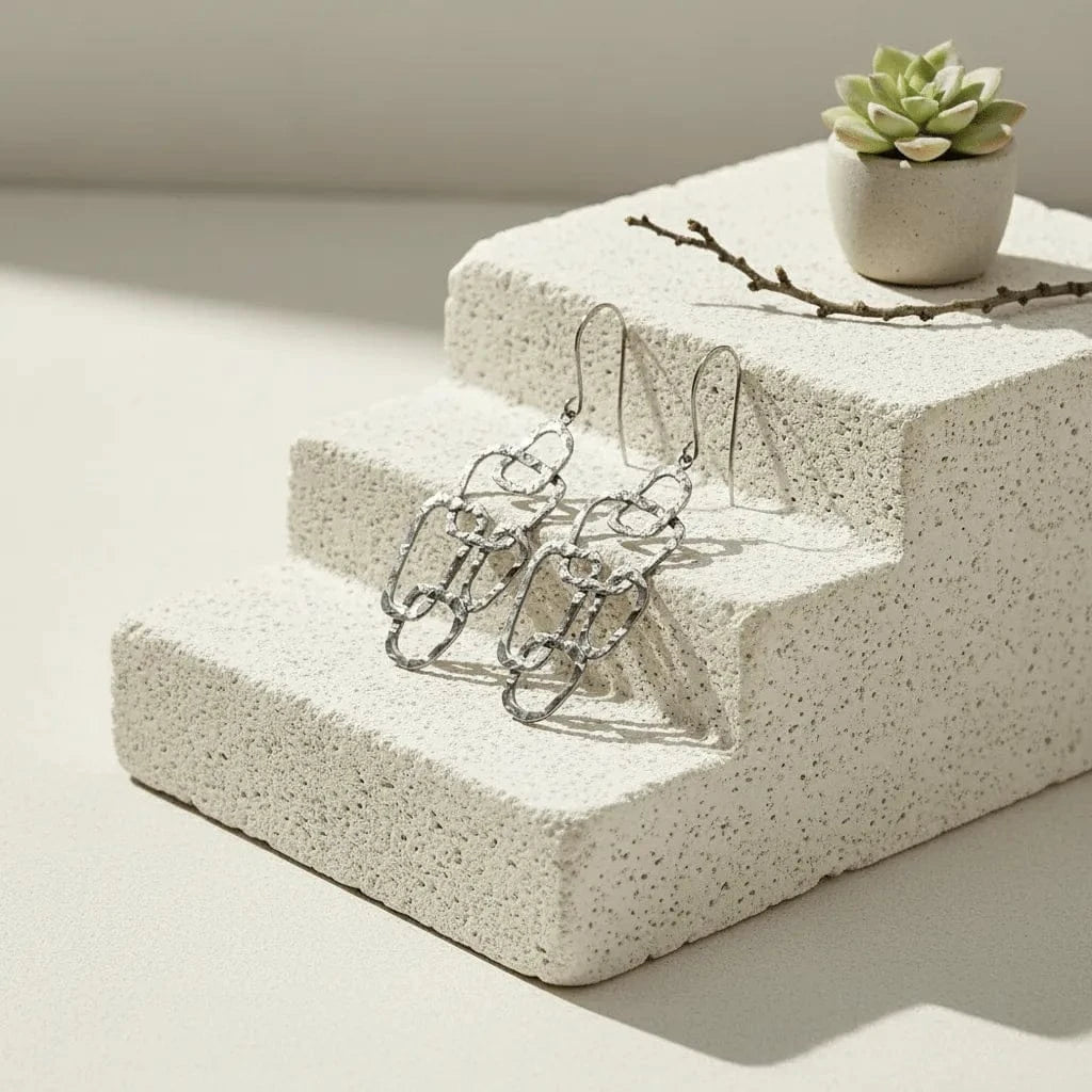 Silver chain earrings on a concrete block with a small plant in the background
