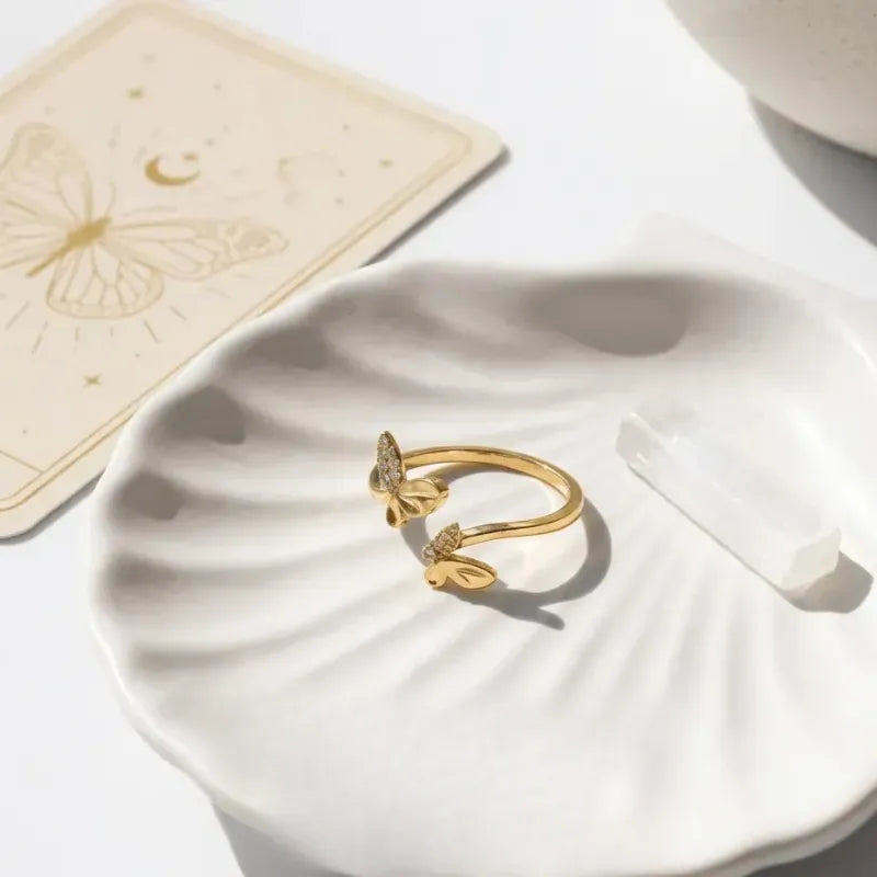 Gold butterfly ring on a white shell with a beige card in the background