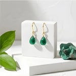 Green teardrop earrings on a white stand with a green crystal and leaves in the background