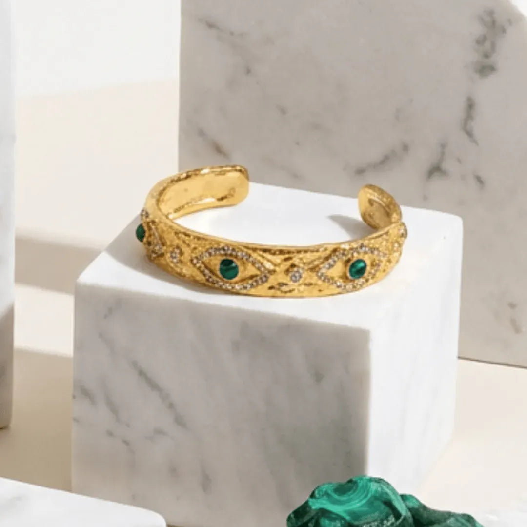 Gold bracelet with green stones on a marble surface