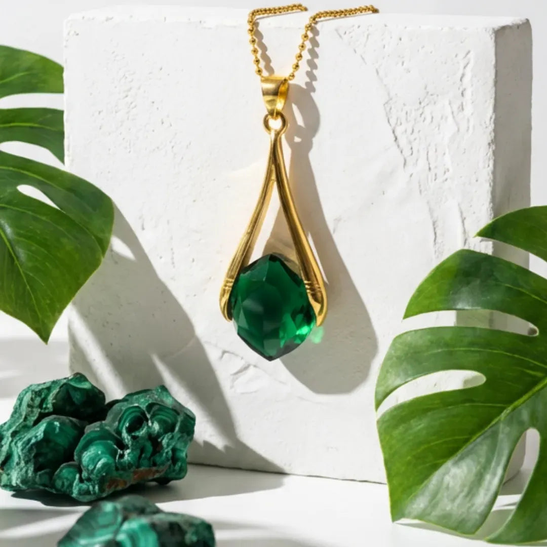 Gold necklace with green pendant on a white surface with green leaves