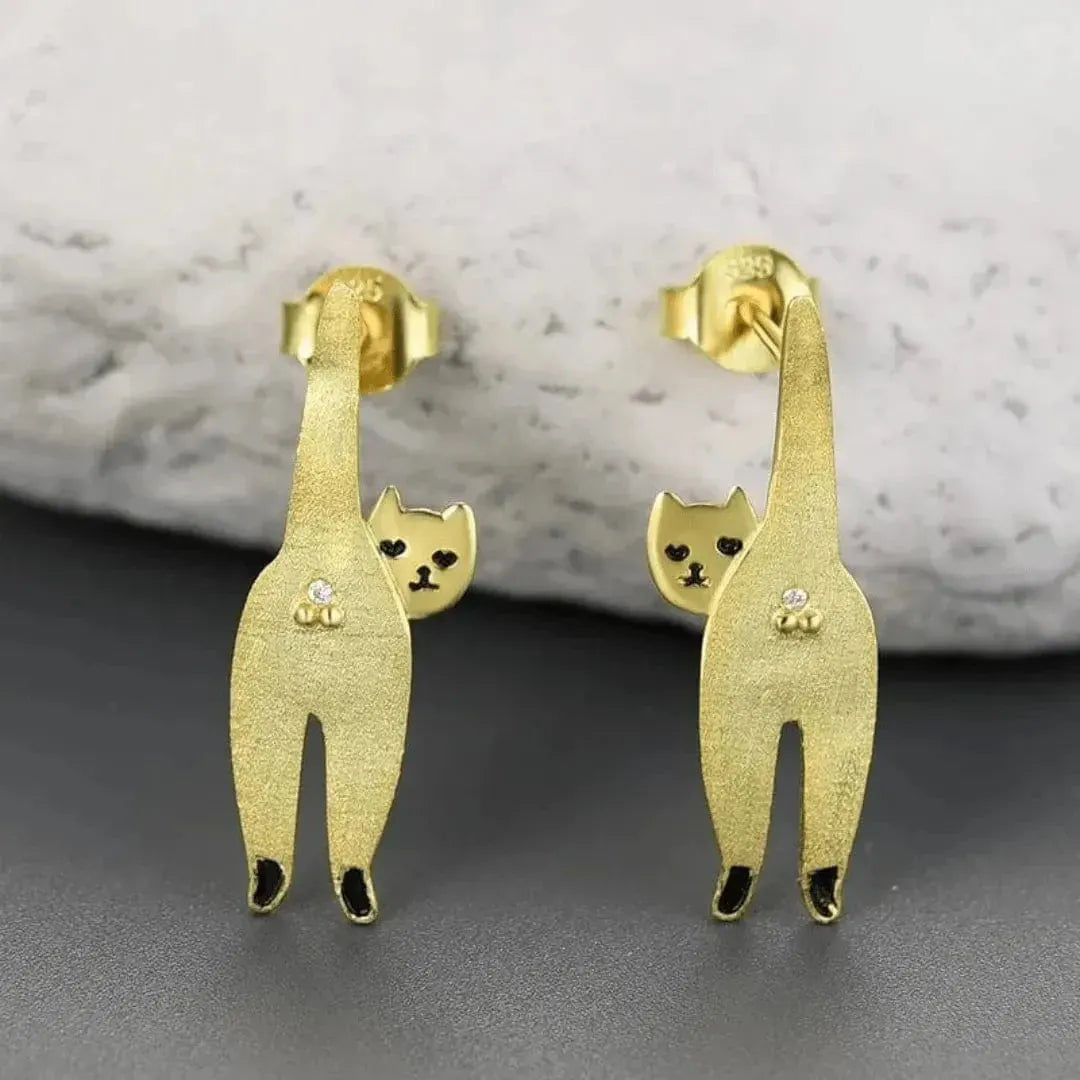 Gold cat-shaped earrings on a gray surface with a marble background