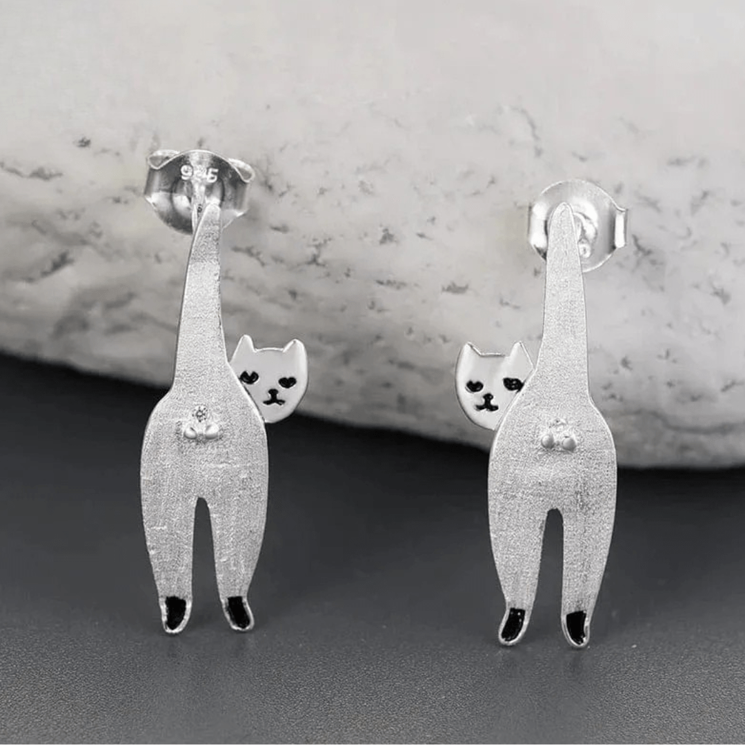 Silver cat-shaped earrings on a gray surface with a marble background