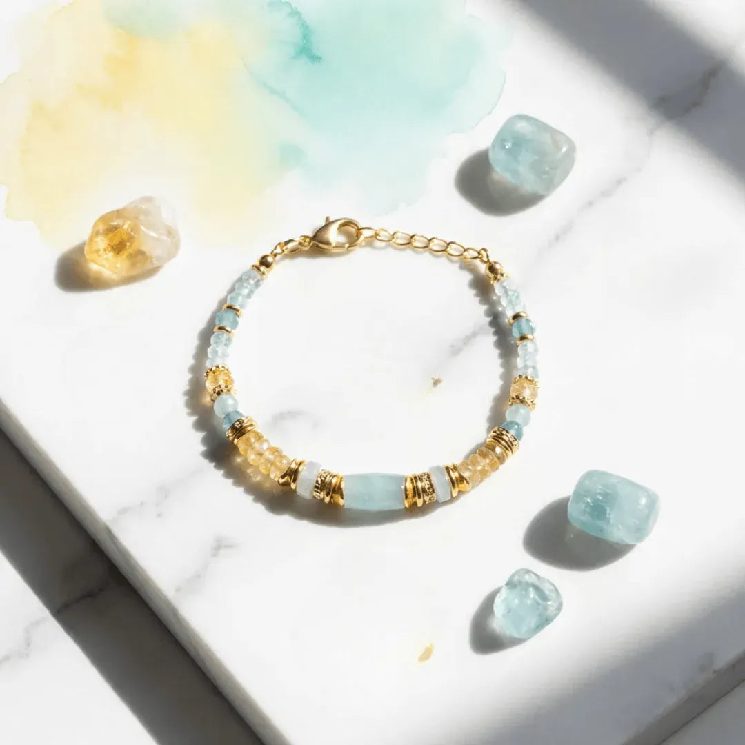 Bracelet with gold and light blue beads on a marble surface with crystals.