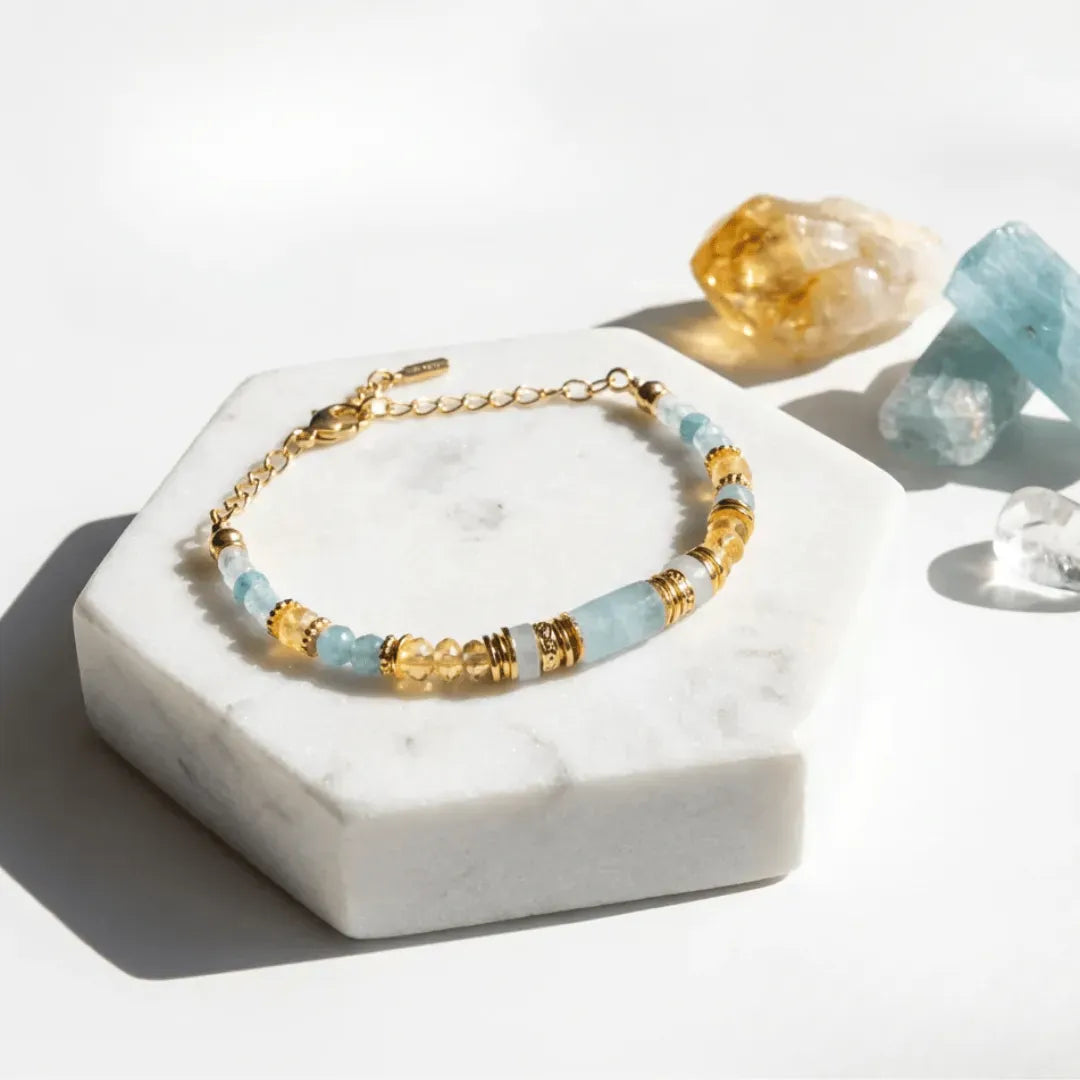 Bracelet with gold and light blue beads on a white marble stand with crystals in the background