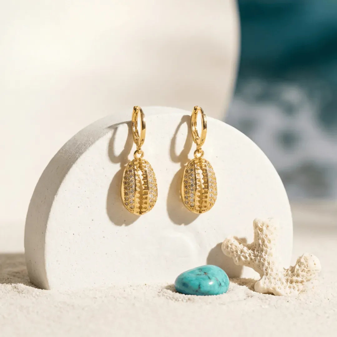 Gold hoop earrings on a white shell with a beach background