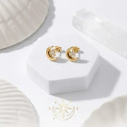 Gold hoop earrings on a white surface with a brand logo in the corner.