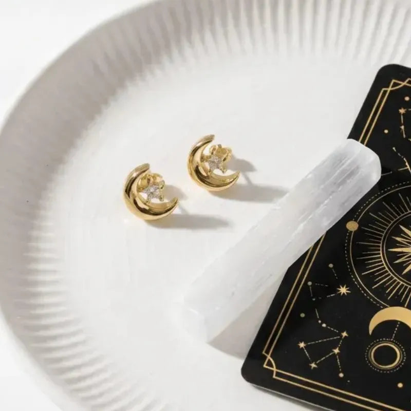 Gold earrings on a white plate with a black card featuring star constellations.