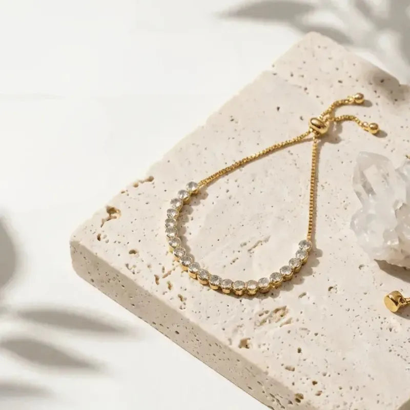 Gold bracelet with clear stones on a beige stone surface