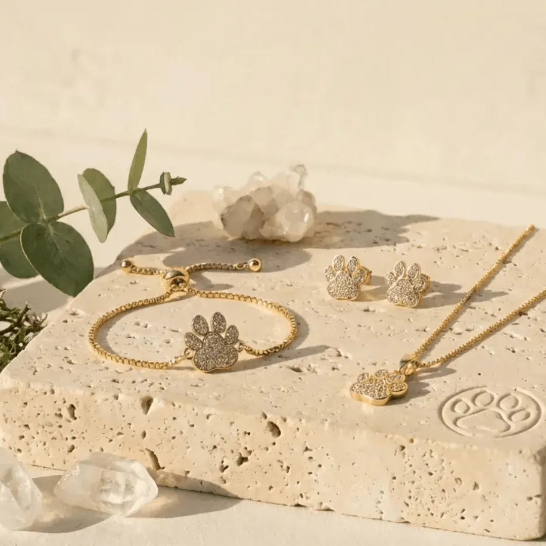 Gold jewelry set including bracelet, necklace, and earrings on a stone surface with crystals and leaves.