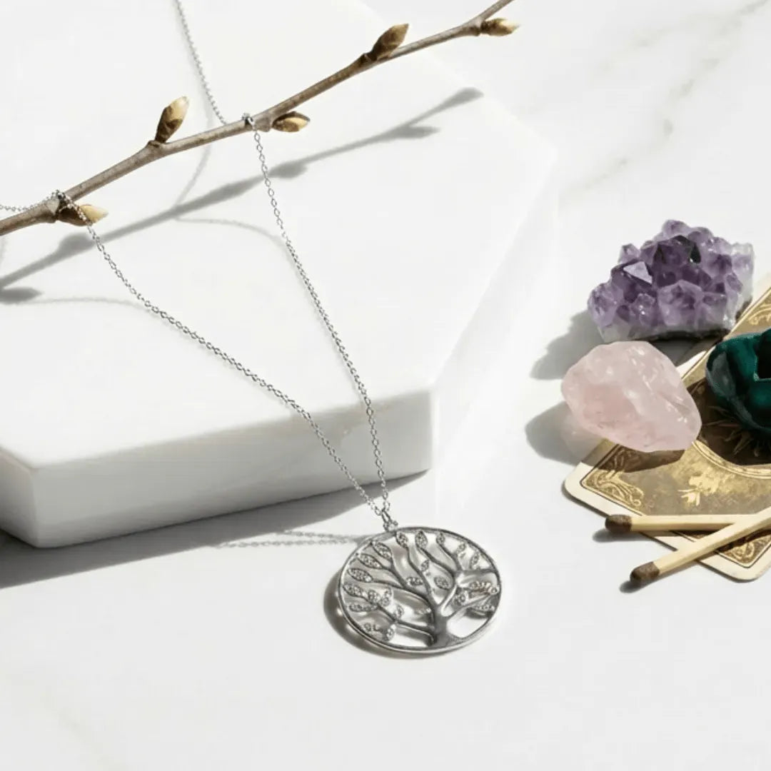 Silver tree pendant necklace on a white surface with crystals and branches.
