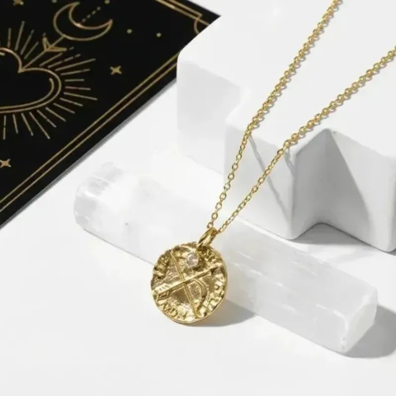 Gold necklace with a circular pendant on a white stand with a black card featuring gold designs.