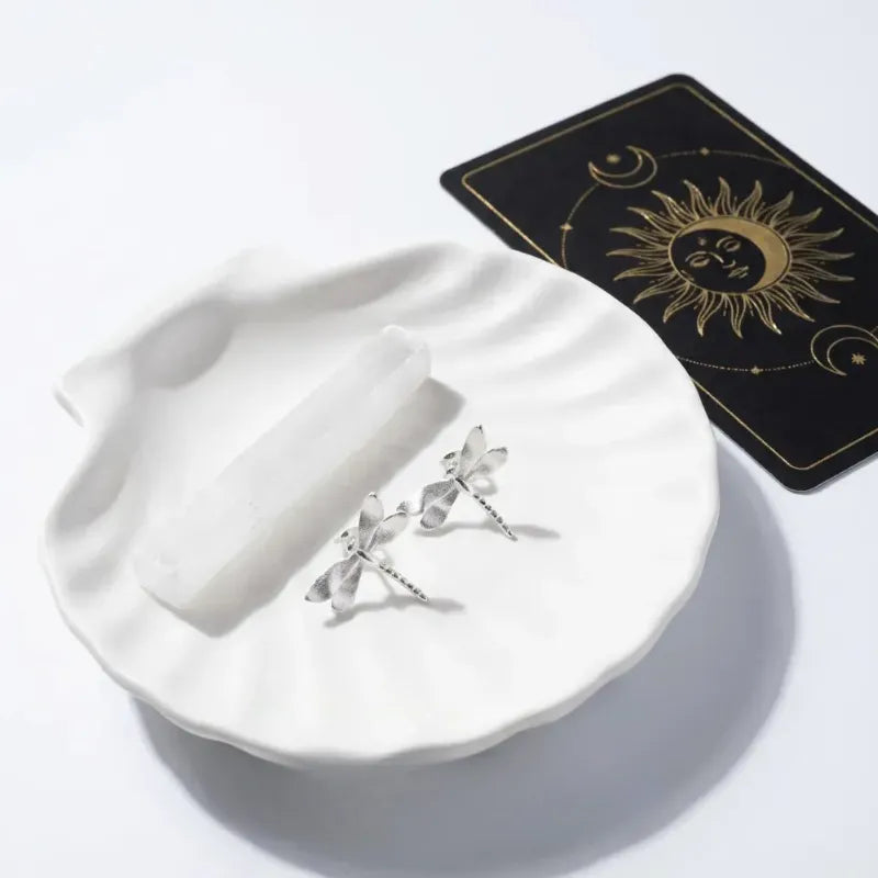 Silver dragonfly earrings on a white dish with a tarot card in the background