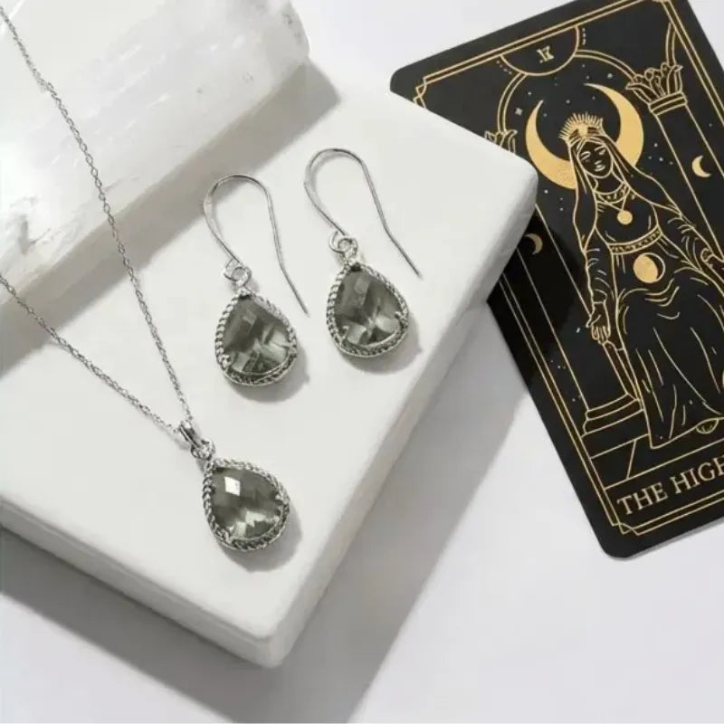 Silver jewelry set with teardrop-shaped stones on a white surface next to a tarot card.