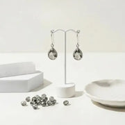Silver teardrop earrings on a white stand with scattered gemstones on a light background