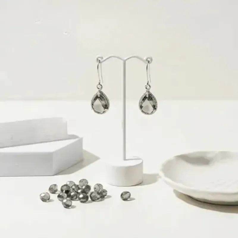 Silver teardrop earrings on a white stand with scattered gemstones on a light background