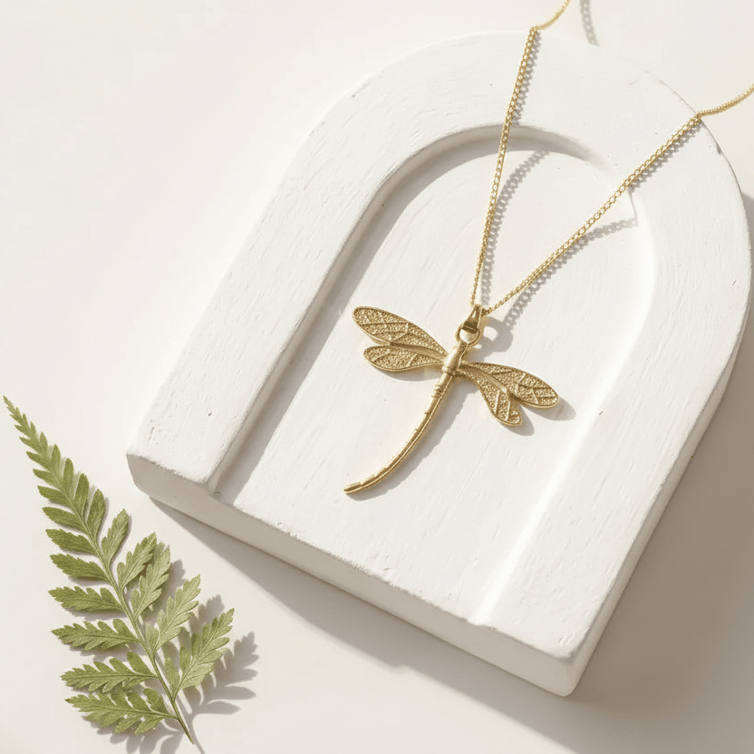 Gold dragonfly necklace on a white heart-shaped stand with a leaf on a light background