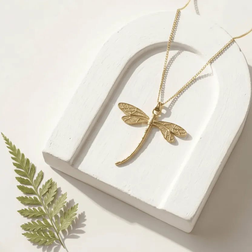 Gold dragonfly necklace on a white heart-shaped stand with a leaf on a light background
