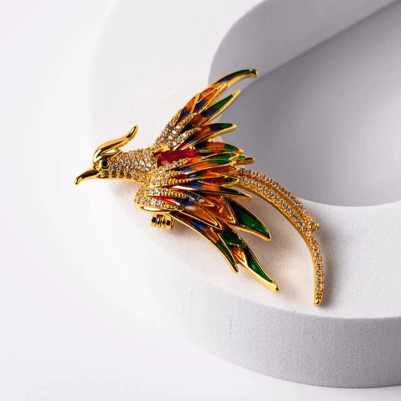 Gold bird-shaped brooch with colorful details on a white stand
