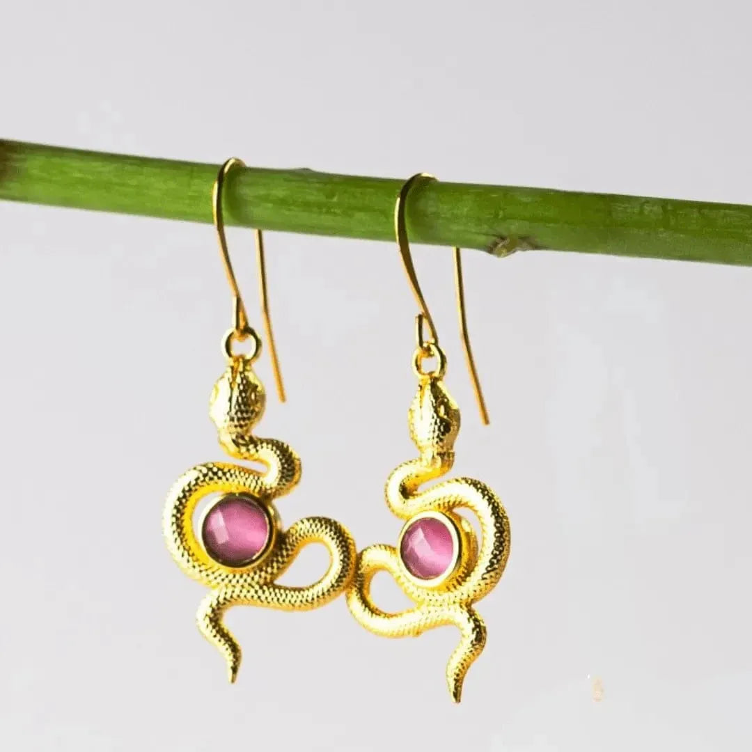 Gold snake-shaped earrings with pink stones on a branch