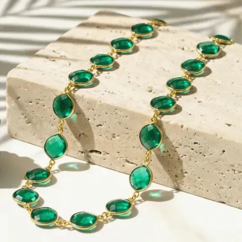 Green necklace with gold chain on a beige stone surface