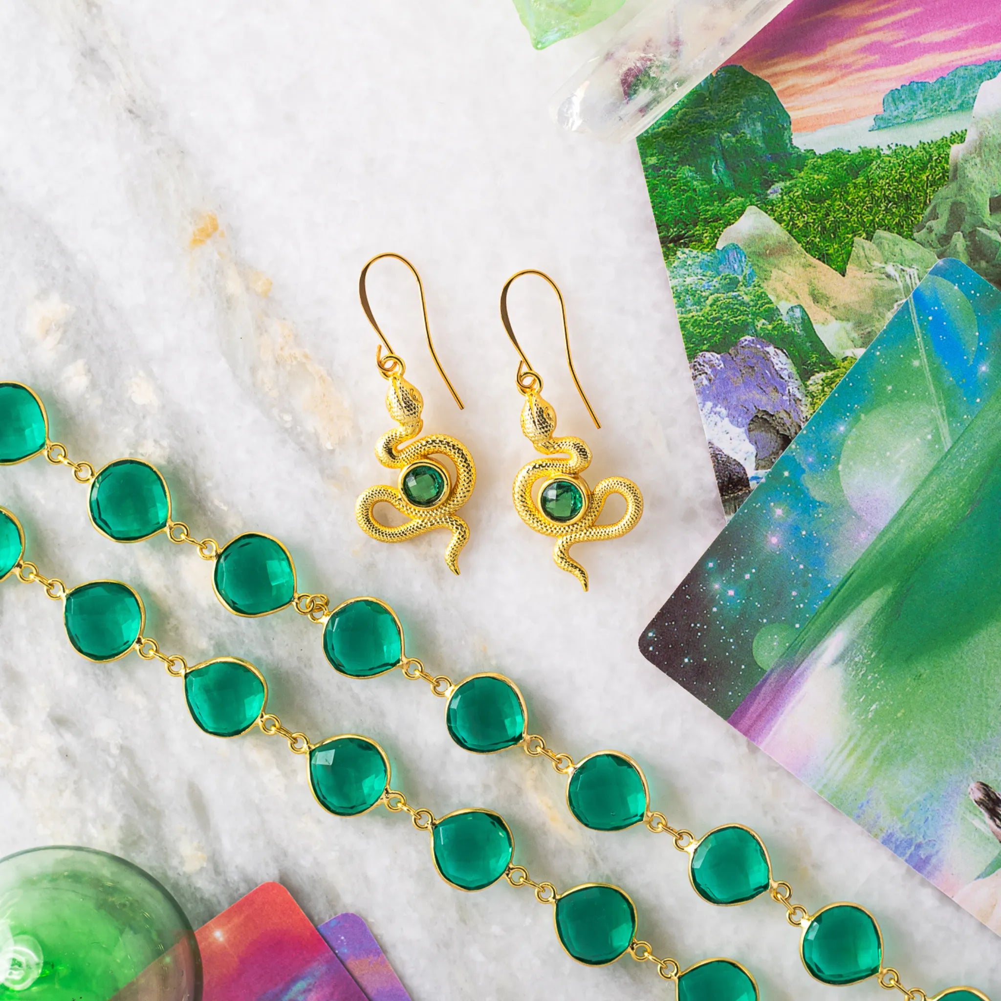 A pair of detailed gold-plated snake earrings adorned with faceted emerald green quartz gemstones