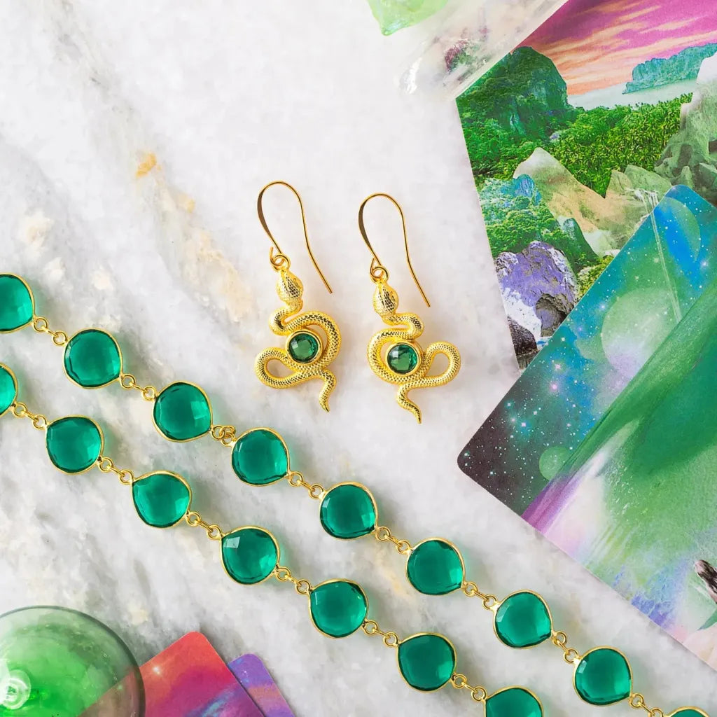A pair of detailed gold-plated snake earrings adorned with faceted emerald green quartz gemstones