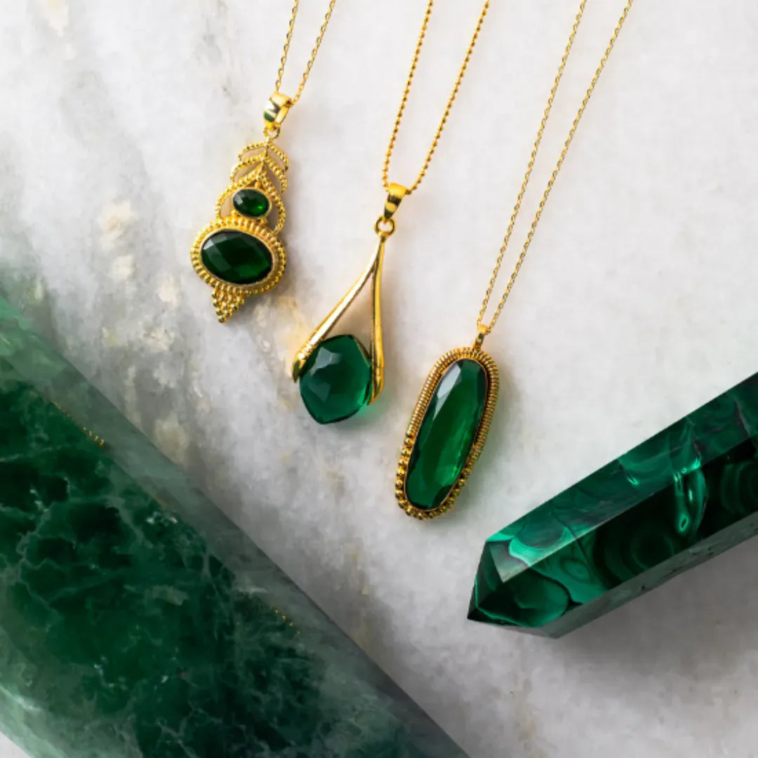 Gold necklaces with green gemstones on a marble surface