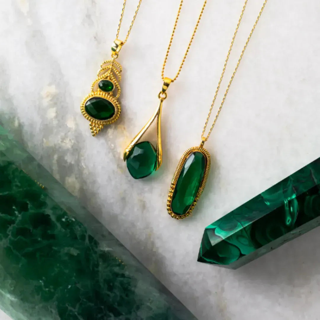 Gold necklaces with green gemstones on a marble surface