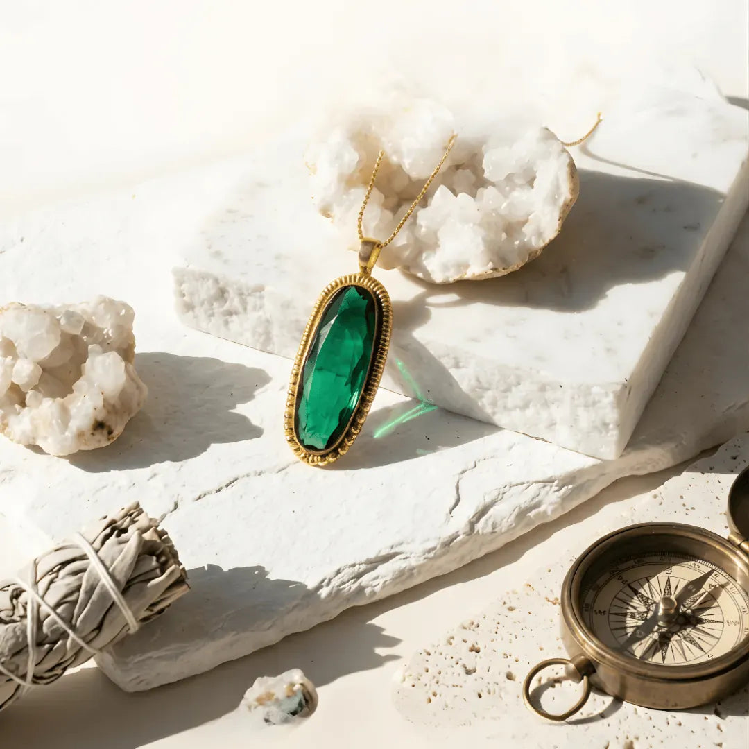 Green pendant necklace on a white stone surface with a compass and sage.