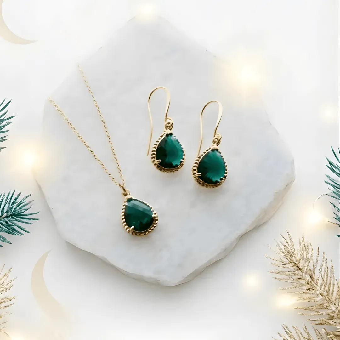 Gold necklace and earrings with green stones on a white surface with decorative elements.