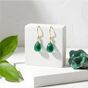 Green teardrop earrings on a white stand with a green crystal and leaves in the background