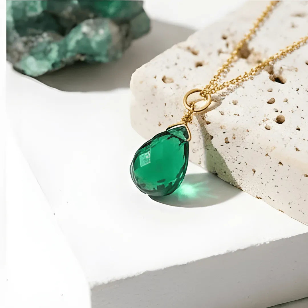 Green teardrop pendant on a gold chain against a textured white surface