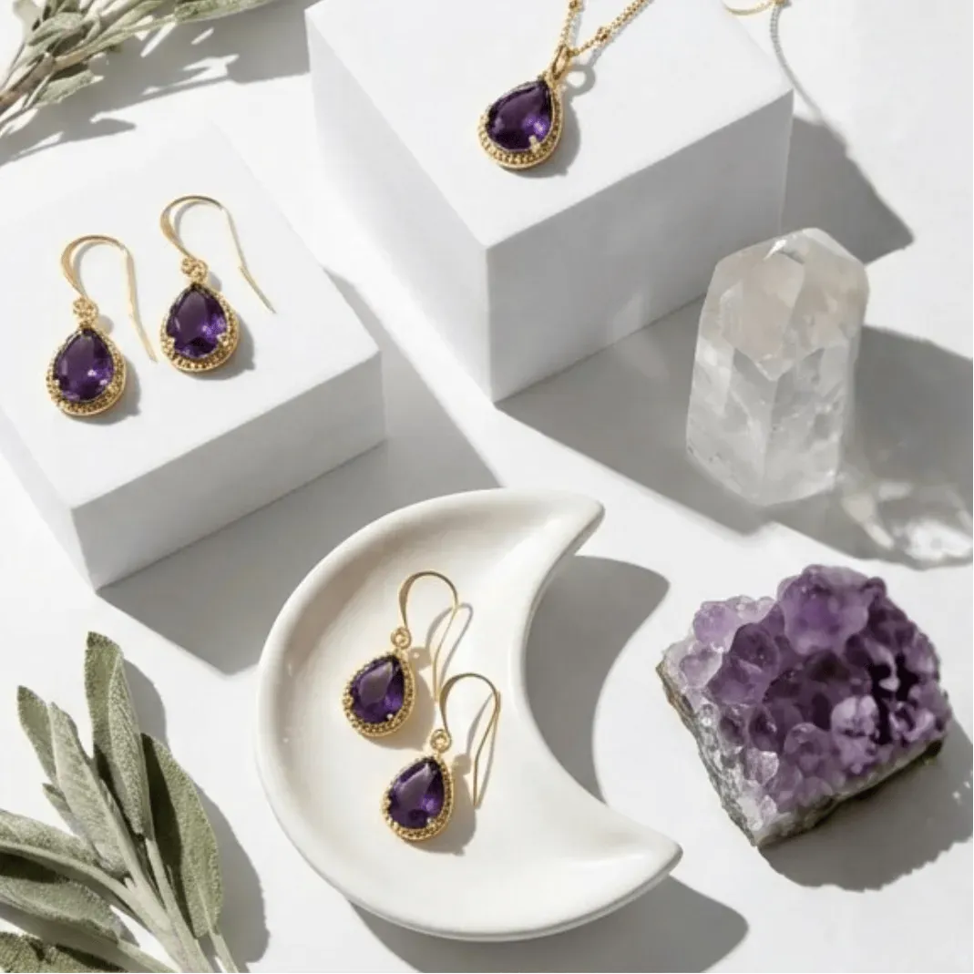 Gold earrings with purple gemstones on a white surface with crystals and plants.