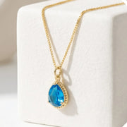 Gold necklace with a blue teardrop pendant on a white surface