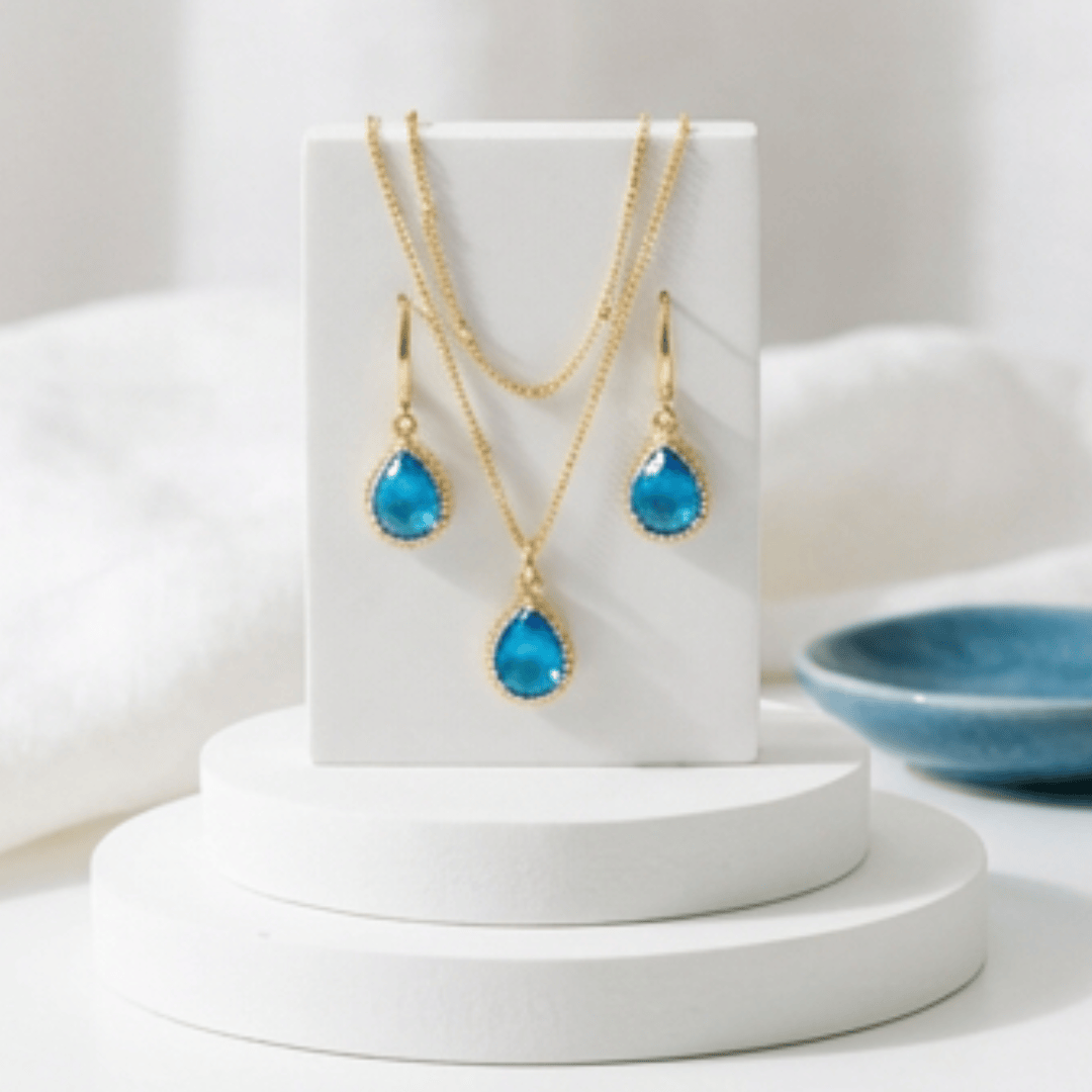 Gold necklace and earrings with blue teardrop stones on a light background