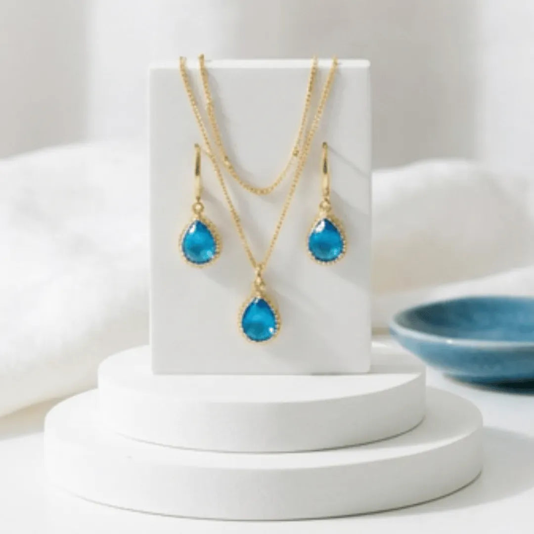 Gold necklace and earrings with blue teardrop stones on a light background