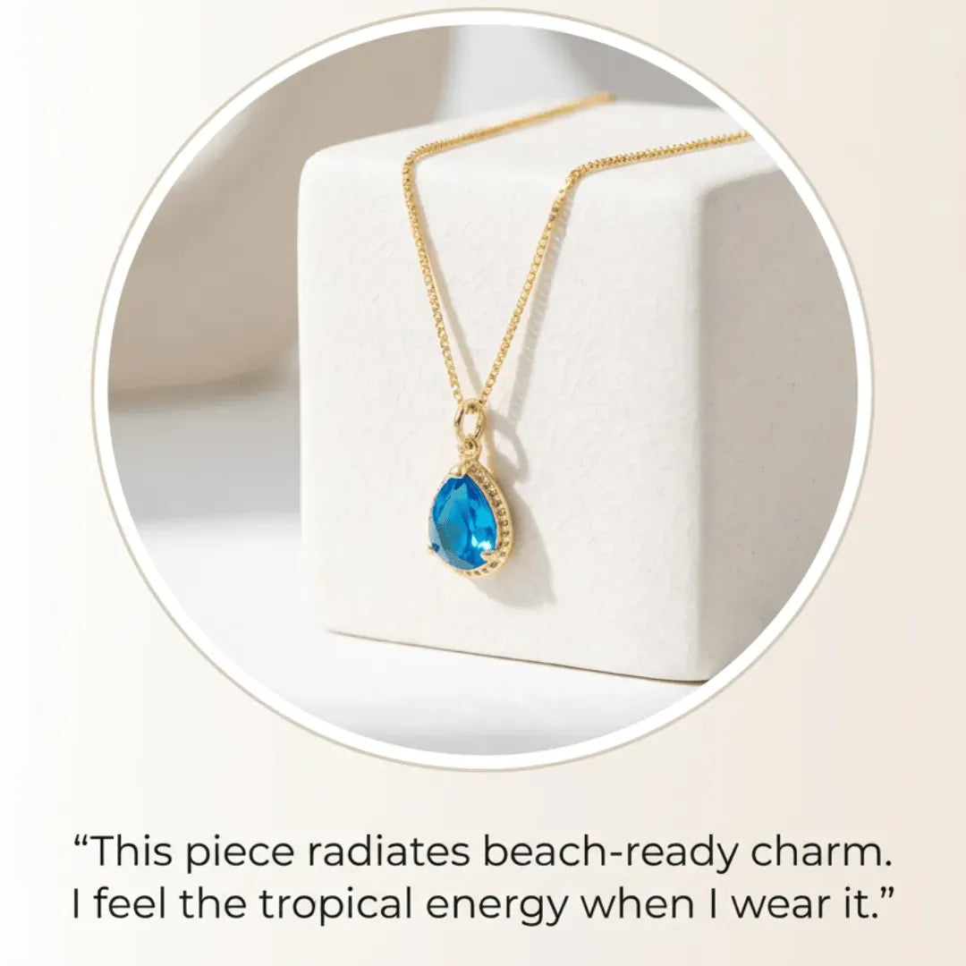 Gold necklace with a blue pendant on a white box, with a quote about beach-ready charm.