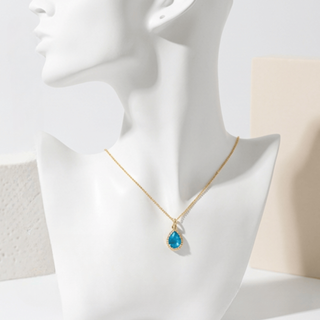 Gold necklace with a blue pendant on a mannequin bust against a neutral background