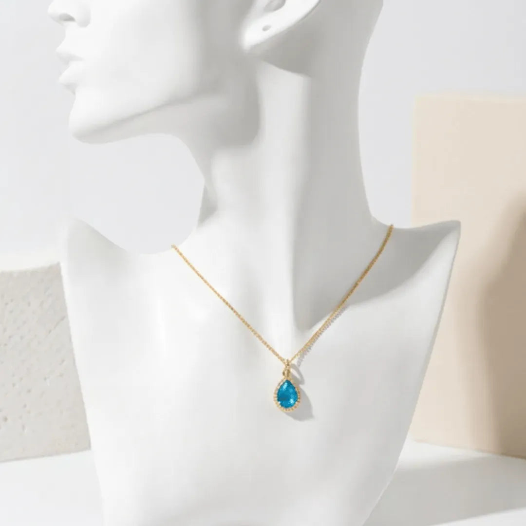 Gold necklace with a blue pendant on a mannequin bust against a neutral background